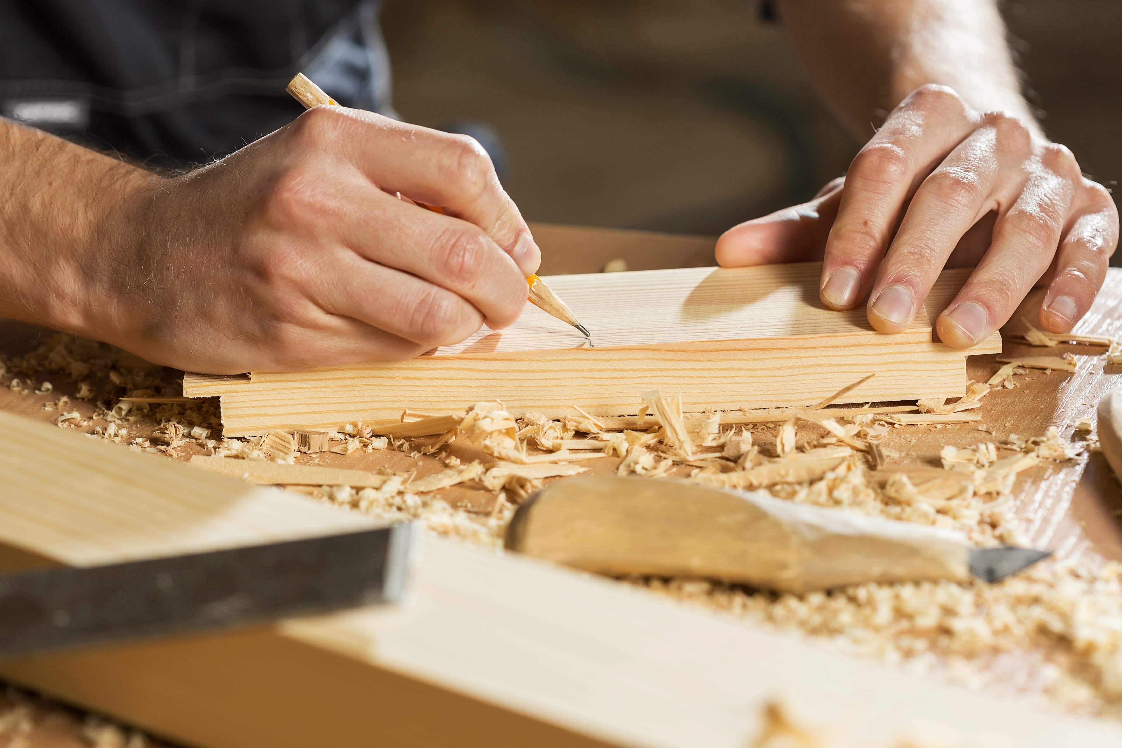 Hands marking a timber board in warm workshop light